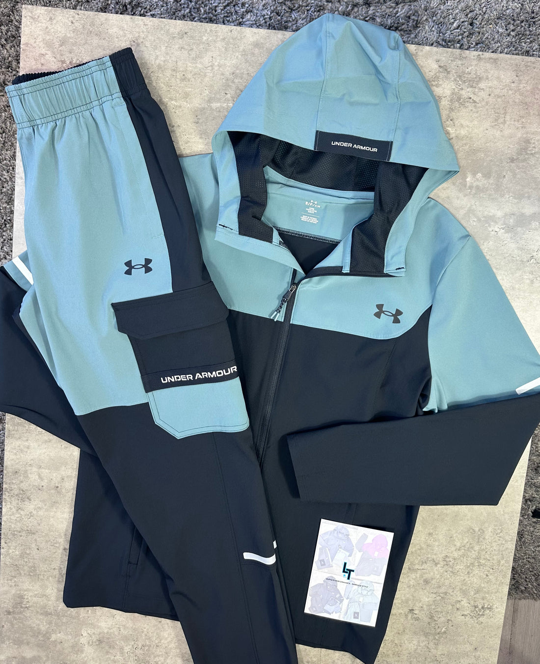 Light blue and black Under Armour jacket and pants on a concrete surface.