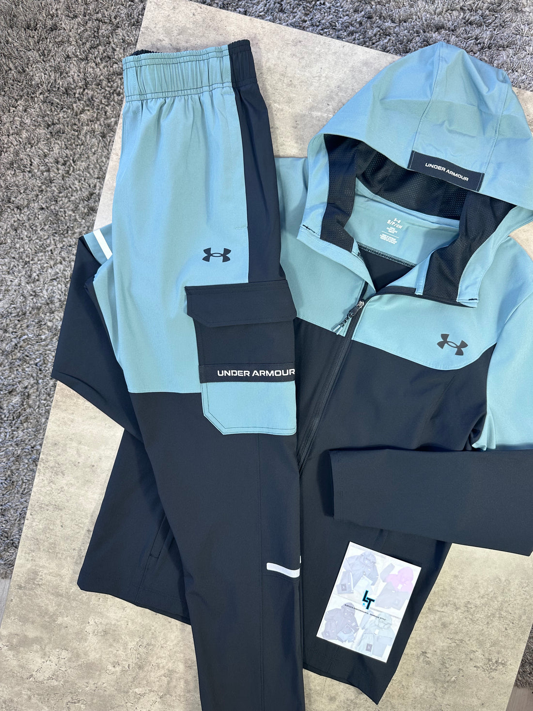 Under Armour athletic wear including a jacket and pants on a concrete surface.